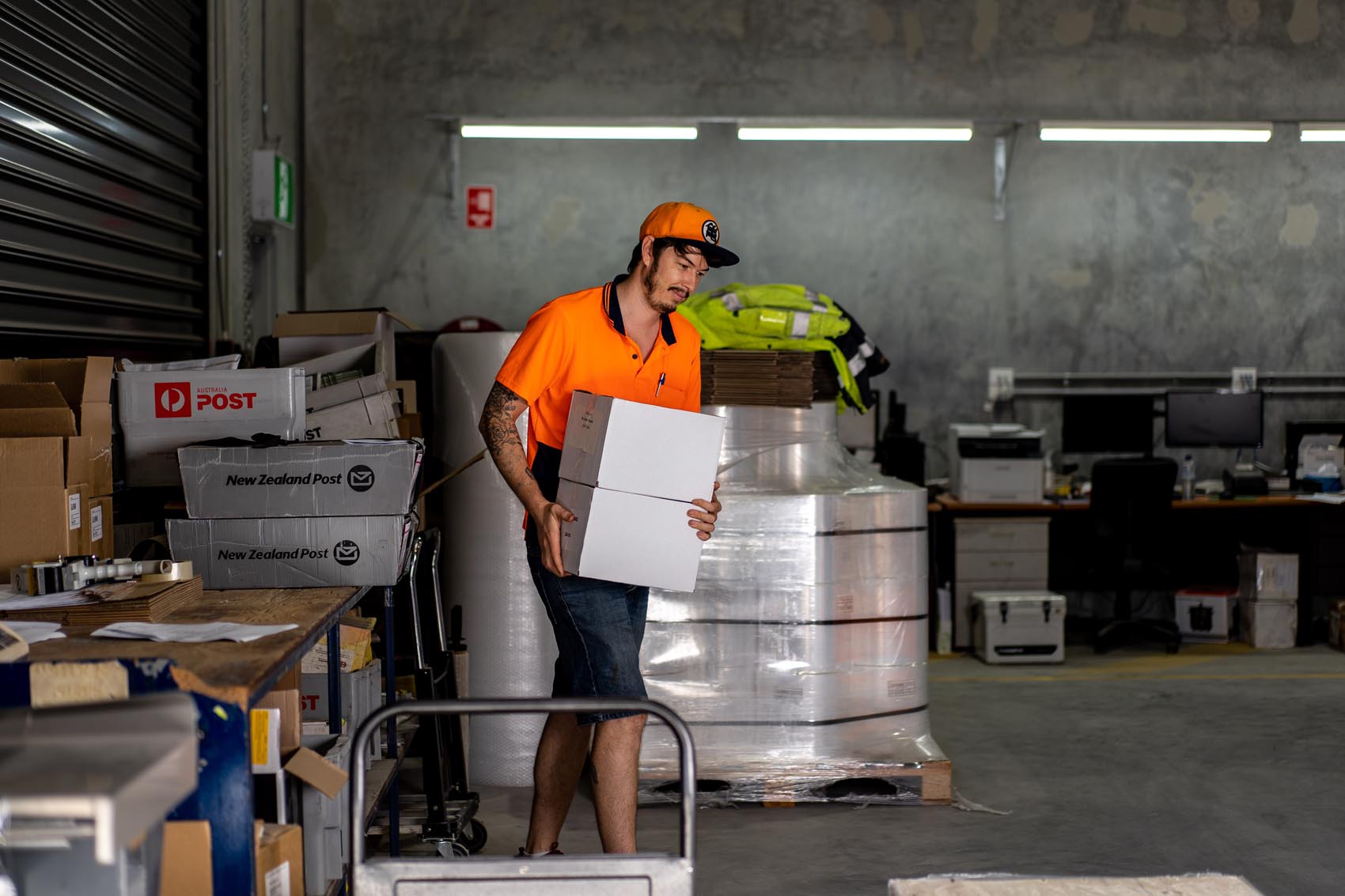 Warehouse team member preparing a delivery with rolls of plastic wrap in the background